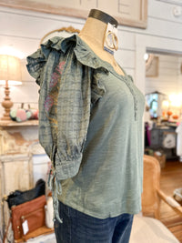 Green blouse with ruffled sleeves on a mannequin in a store setting