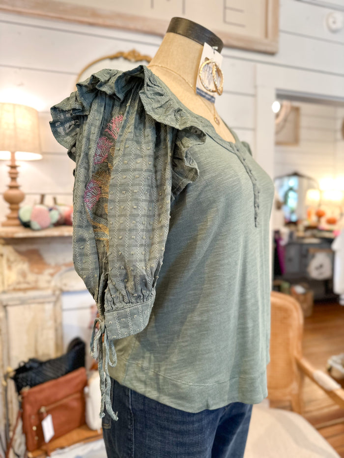 Green blouse with ruffled sleeves on a mannequin in a store setting
