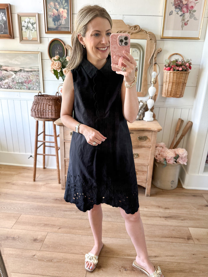 Woman taking a mirror selfie wearing a black dress in a home setting.