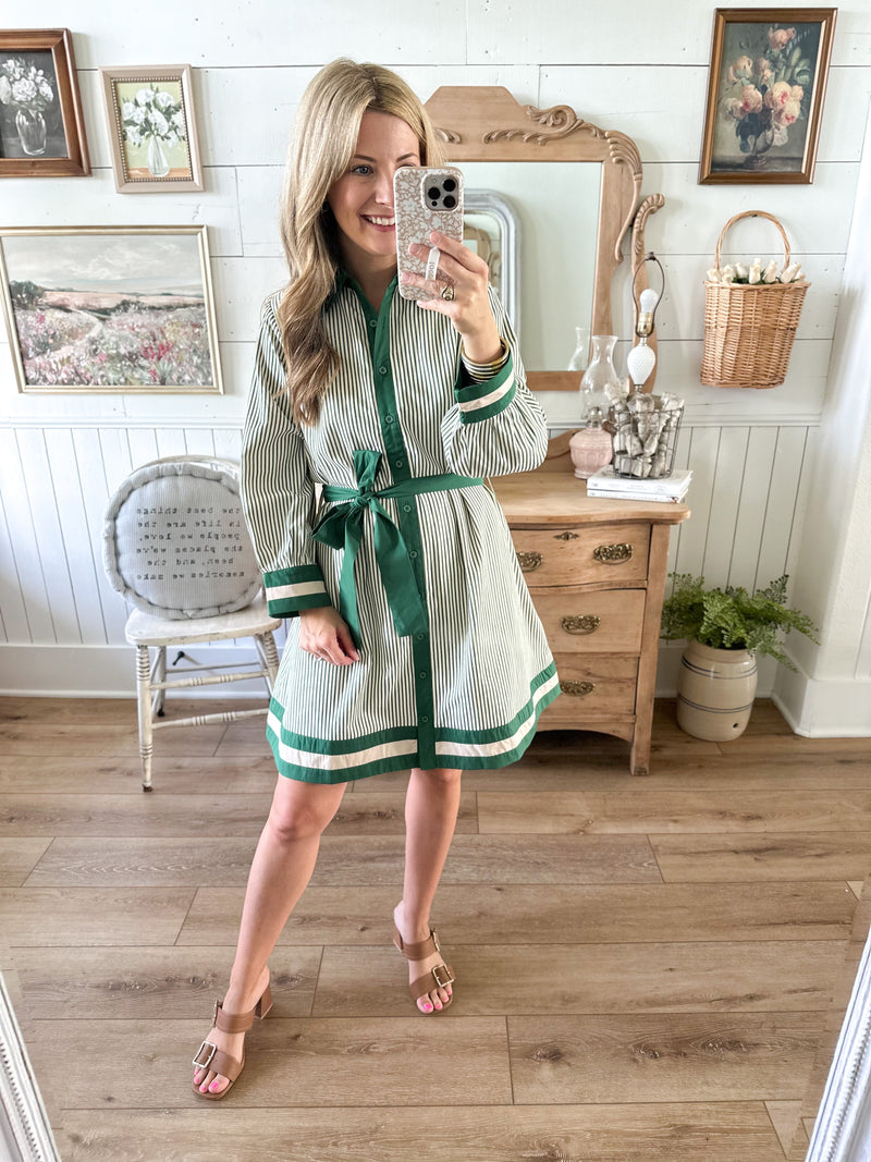 Woman taking a mirror selfie wearing a green and white striped dress with brown heels in a home setting.