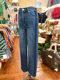 A pair of dark blue wide-leg denim jeans displayed on a mannequin in a clothing boutique. The jeans feature a straight-to-slightly-flared leg, classic five-pocket styling, and double contrast stitching running down the outer seams.
