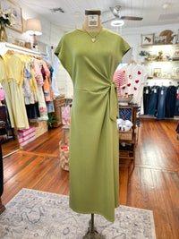 Green dress on a mannequin in a clothing store with various garments in the background.
