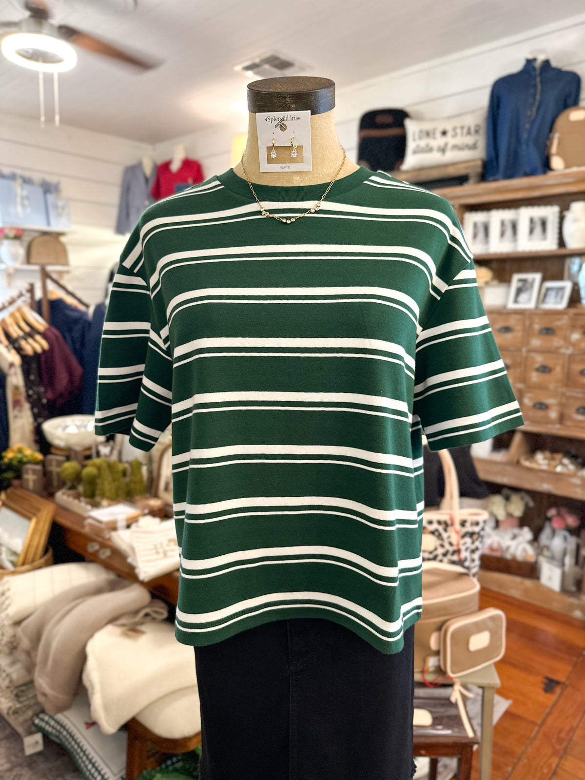 A green and white horizontally striped short-sleeve t-shirt displayed on a mannequin torso inside a clothing boutique.