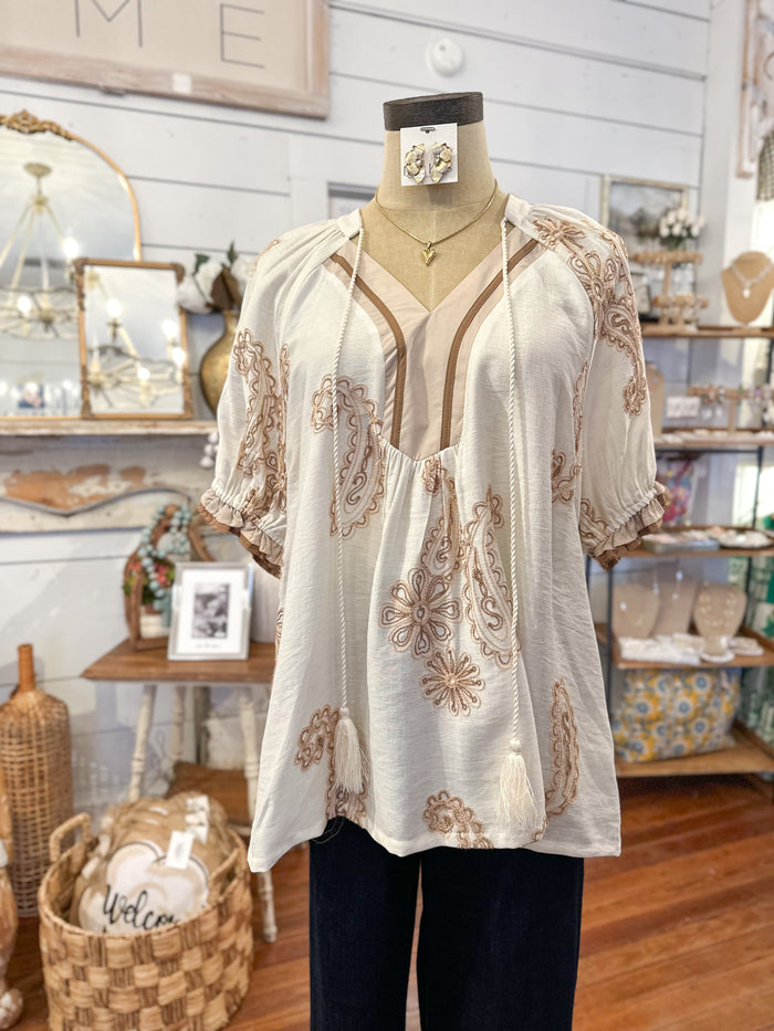 Mannequin wearing a white blouse with brown embroidery in a store setting