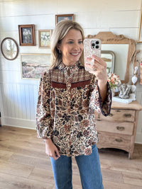 Woman taking a mirror selfie wearing a patterned blouse and jeans in a home setting.