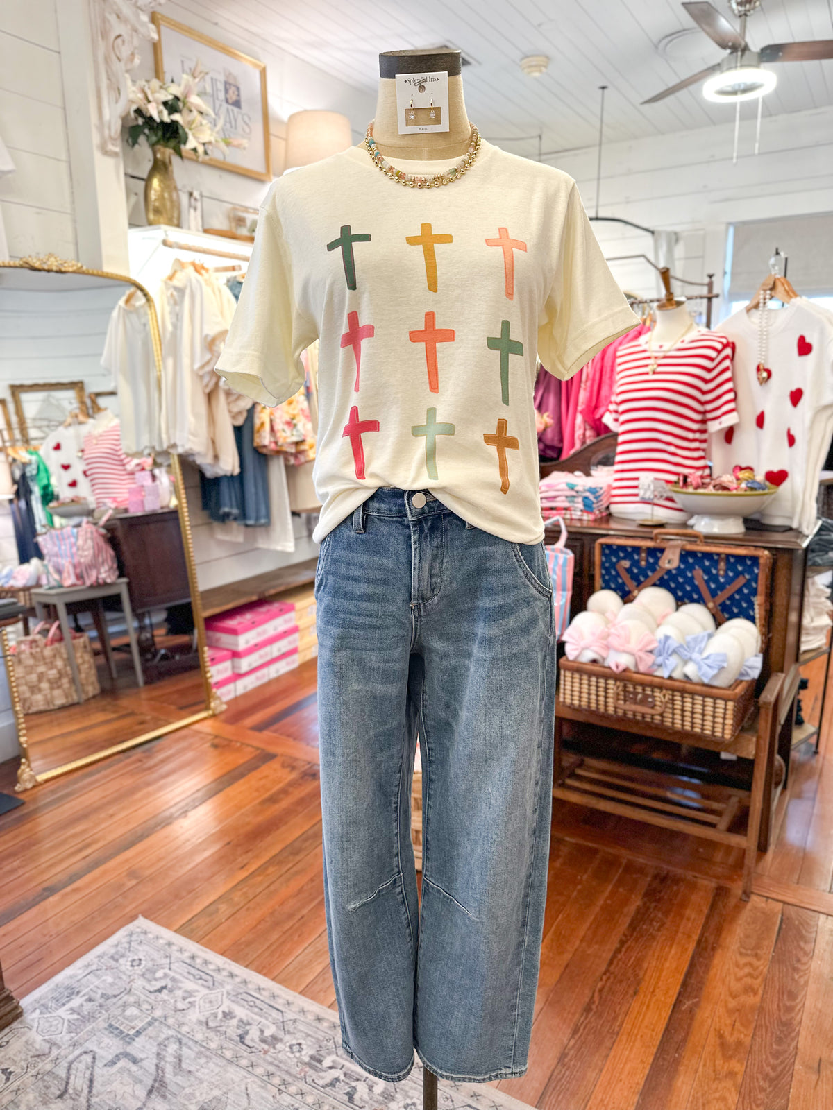 Mannequin wearing a cream t-shirt with colorful cross patterns and blue jeans in a store setting.