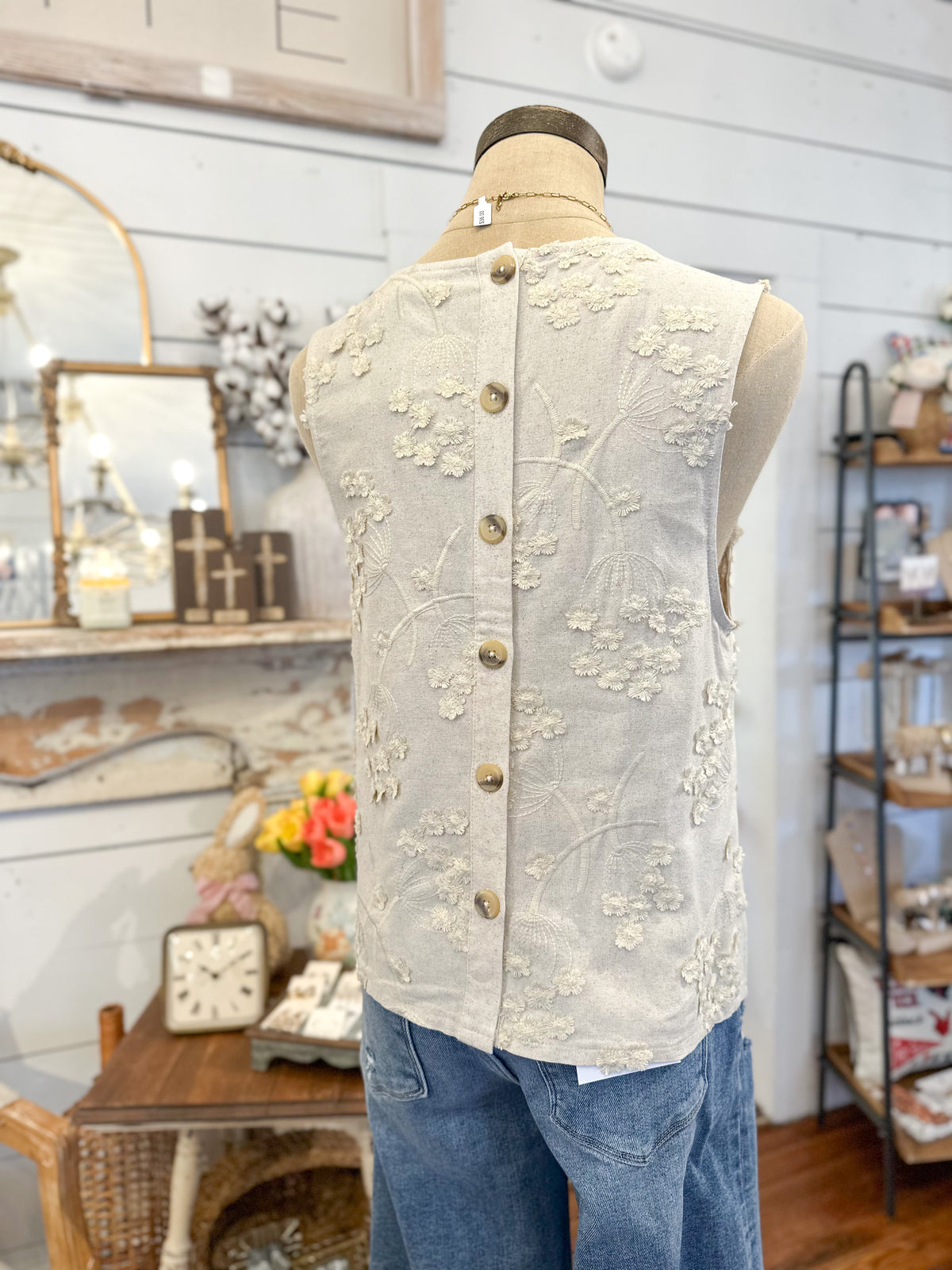 Mannequin wearing a floral embroidered top in a store setting back showing buttons 
