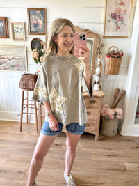 Woman taking a mirror selfie in a home setting, wearing a beige top with star patterns and denim shorts.
