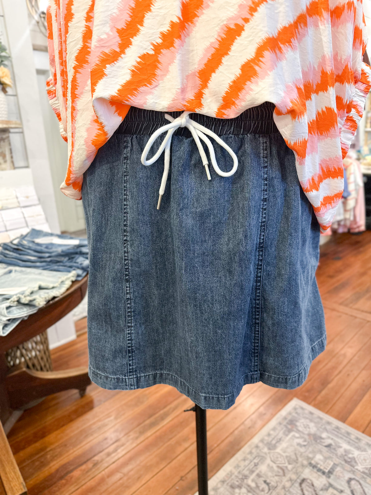 Denim skirt on a mannequin with an orange and white striped shirt in a store setting