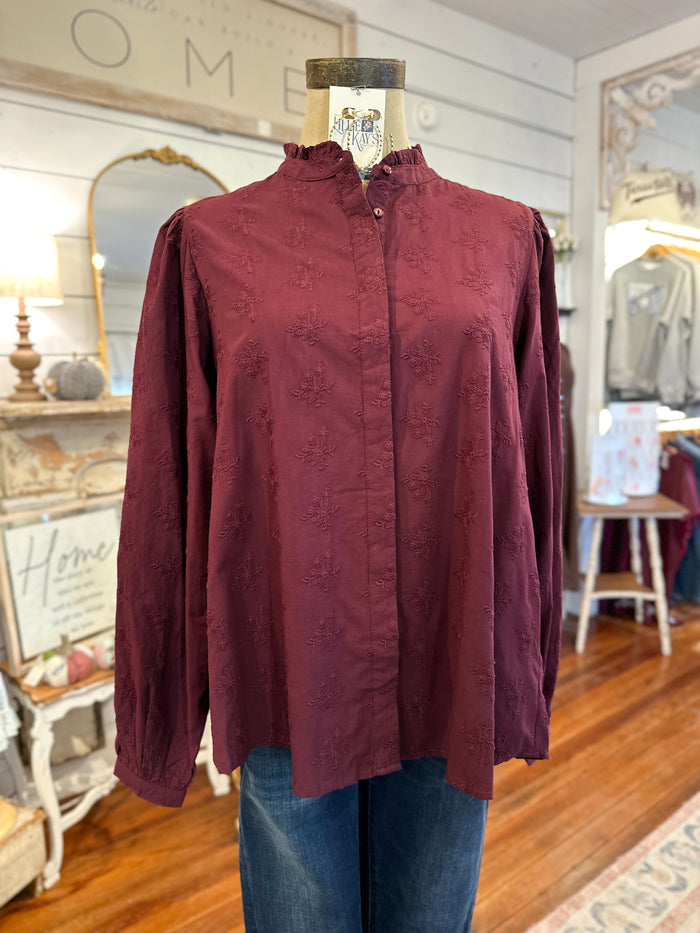 Maroon blouse on a mannequin in a store setting with decor elements.