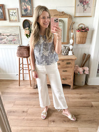 Woman taking a mirror selfie in a room with wooden floor and decor. embroidered top with black checkered print 