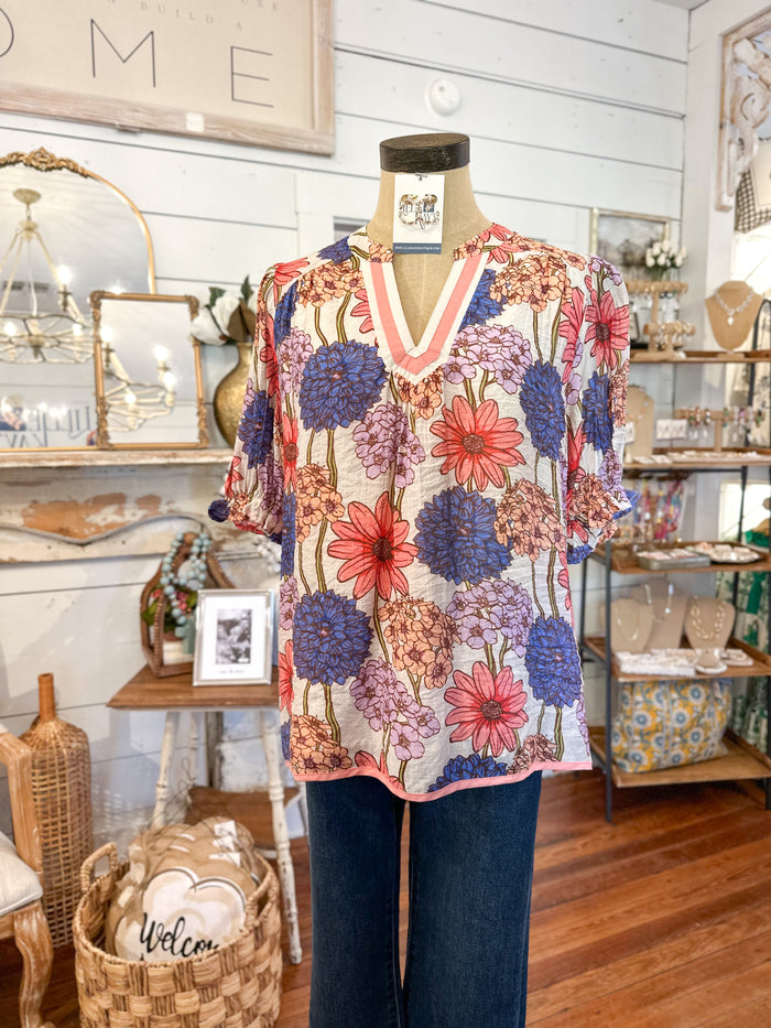 Mannequin wearing a floral top in a store setting with various decor items.