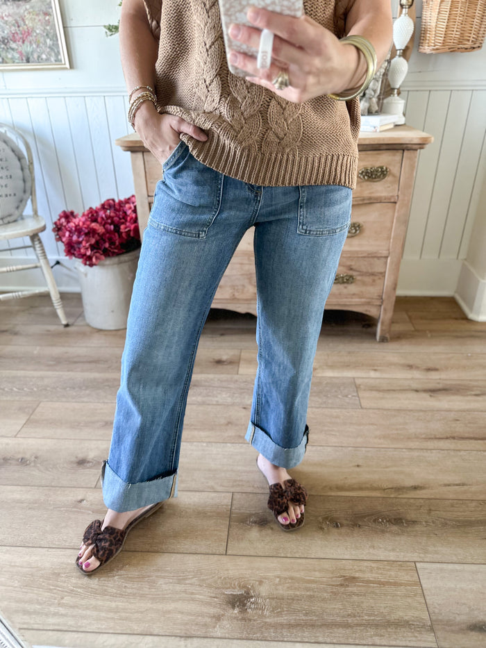 Person wearing a brown cable knit sweater and blue jeans standing on a wooden floor.
