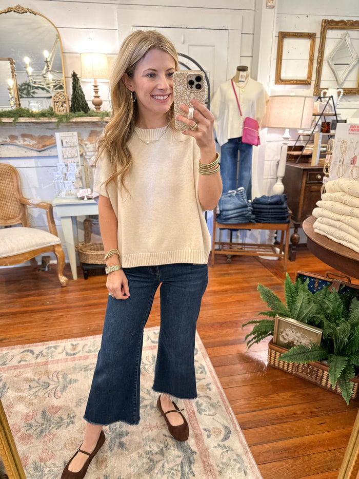 Woman taking a mirror selfie in a store, wearing a beige sweater and blue jeans.