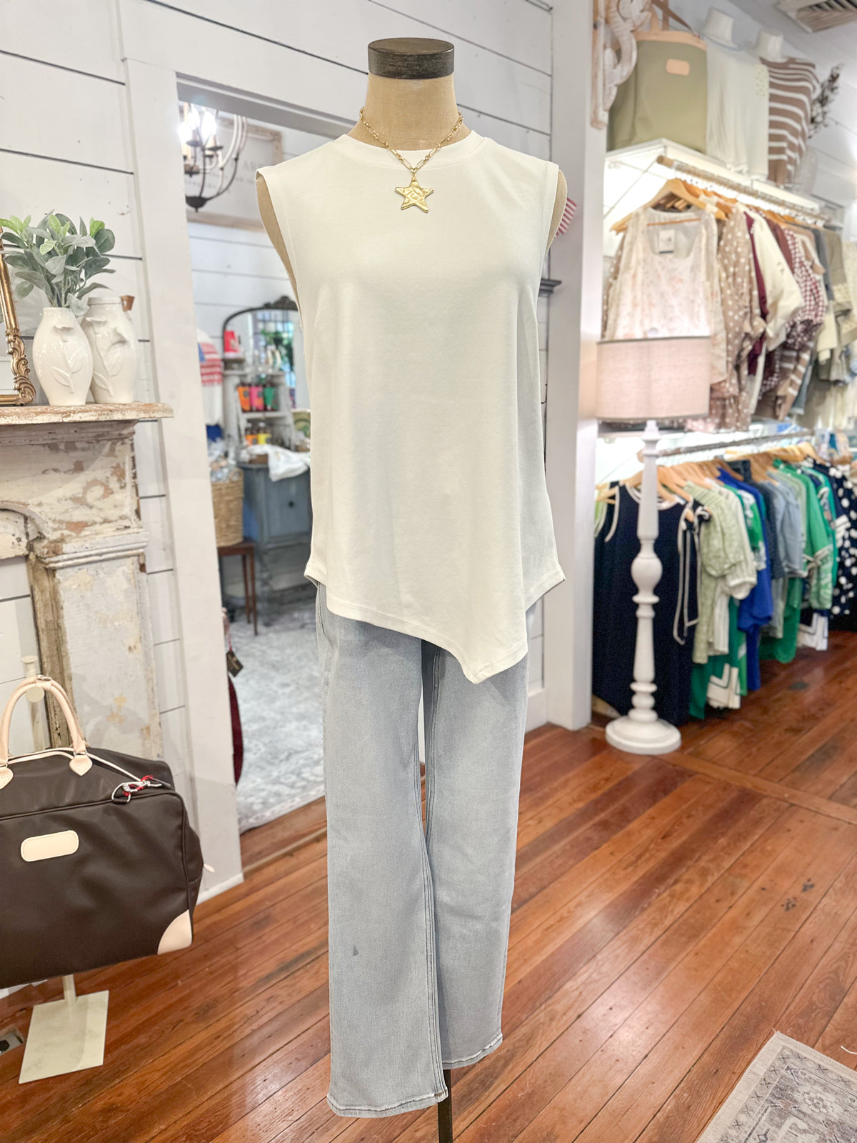 Mannequin wearing a white sleeveless top and light blue jeans in a store setting with clothing racks and decor.