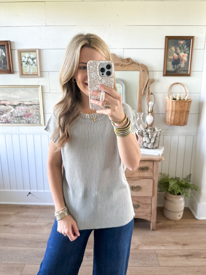 Woman taking a mirror selfie in a room with wooden floor and white walls. light weight grey sweater with white trim details 