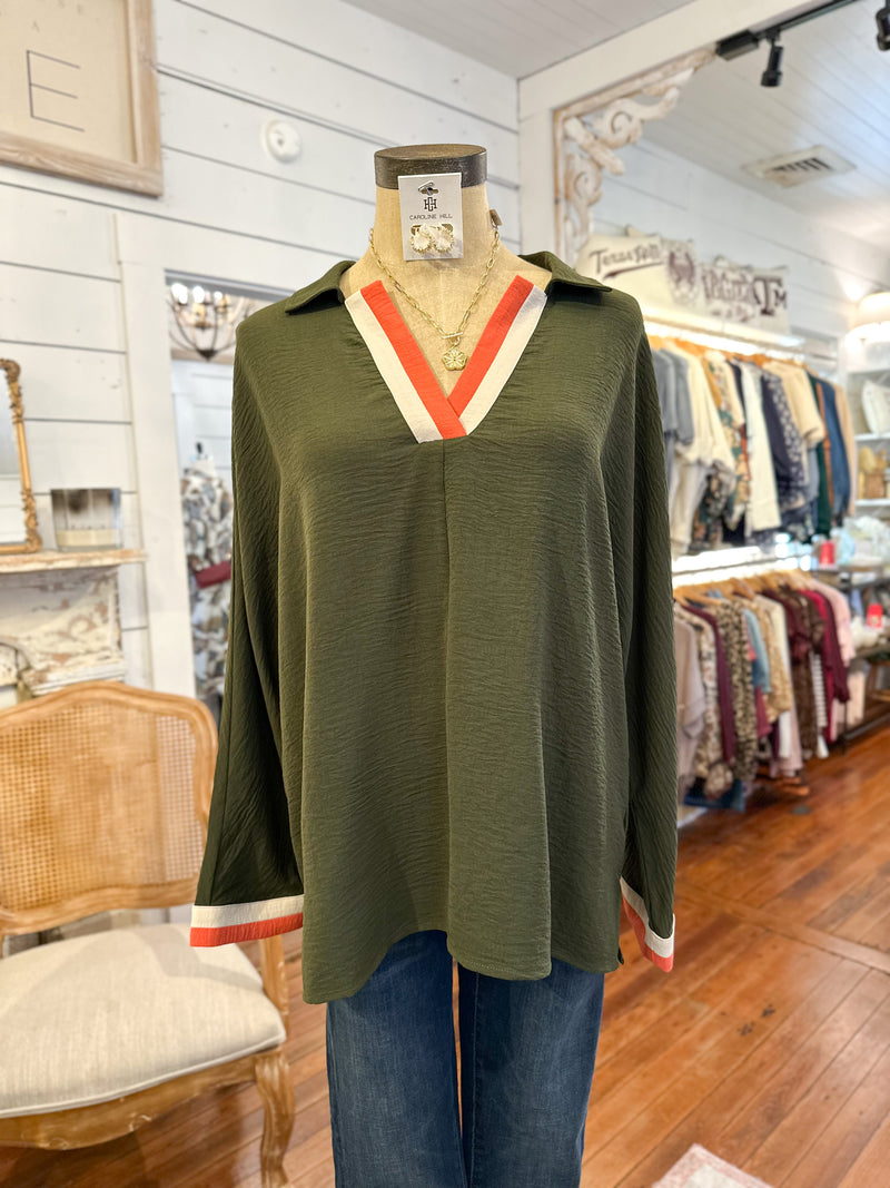 Green long-sleeve top with red and white trim on a mannequin in a store setting.