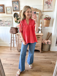 Woman taking a mirror selfie wearing a coral blouse and blue jeans in a home setting.