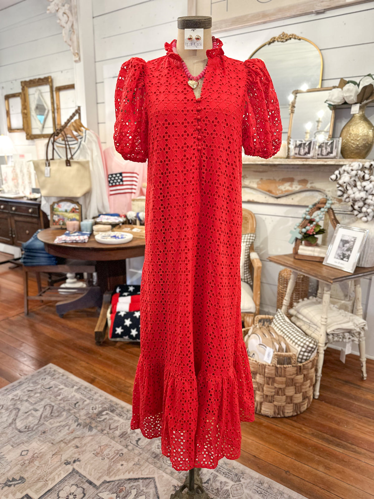 Red eyelet lace dress on a mannequin in a room with wooden floors and decorative items.