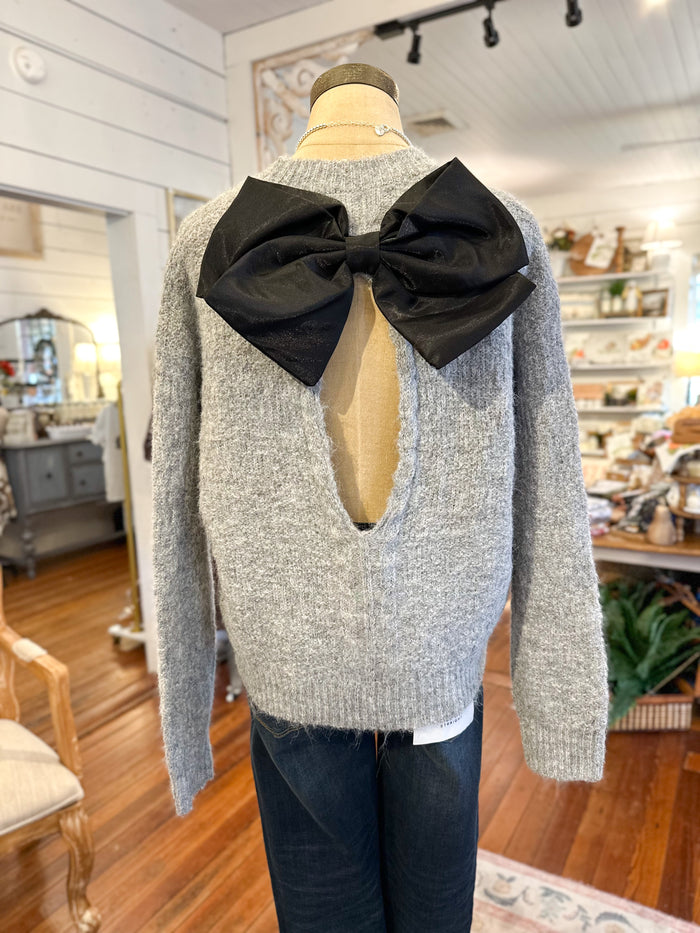 Mannequin wearing a gray sweater with a large black bow at the back in a store setting.