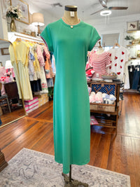 Green dress on a mannequin in a store setting with various clothing items in the background.