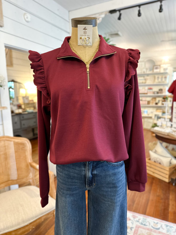 Maroon pullover with ruffled shoulders on a mannequin in a store setting