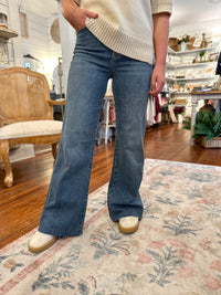 Person wearing blue flared jeans and a cream sweater in a home setting.