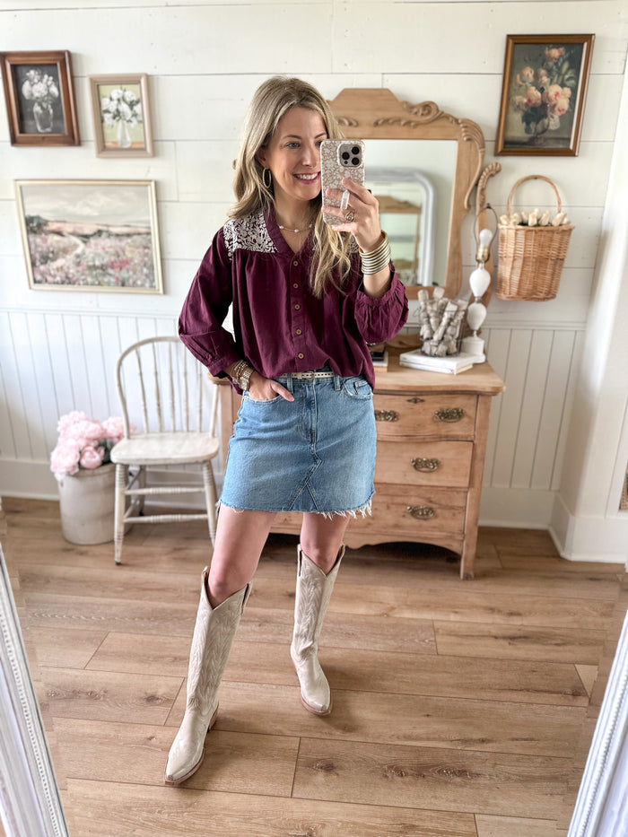 Woman taking a mirror selfie in a room with wooden floors and framed pictures on the wall.