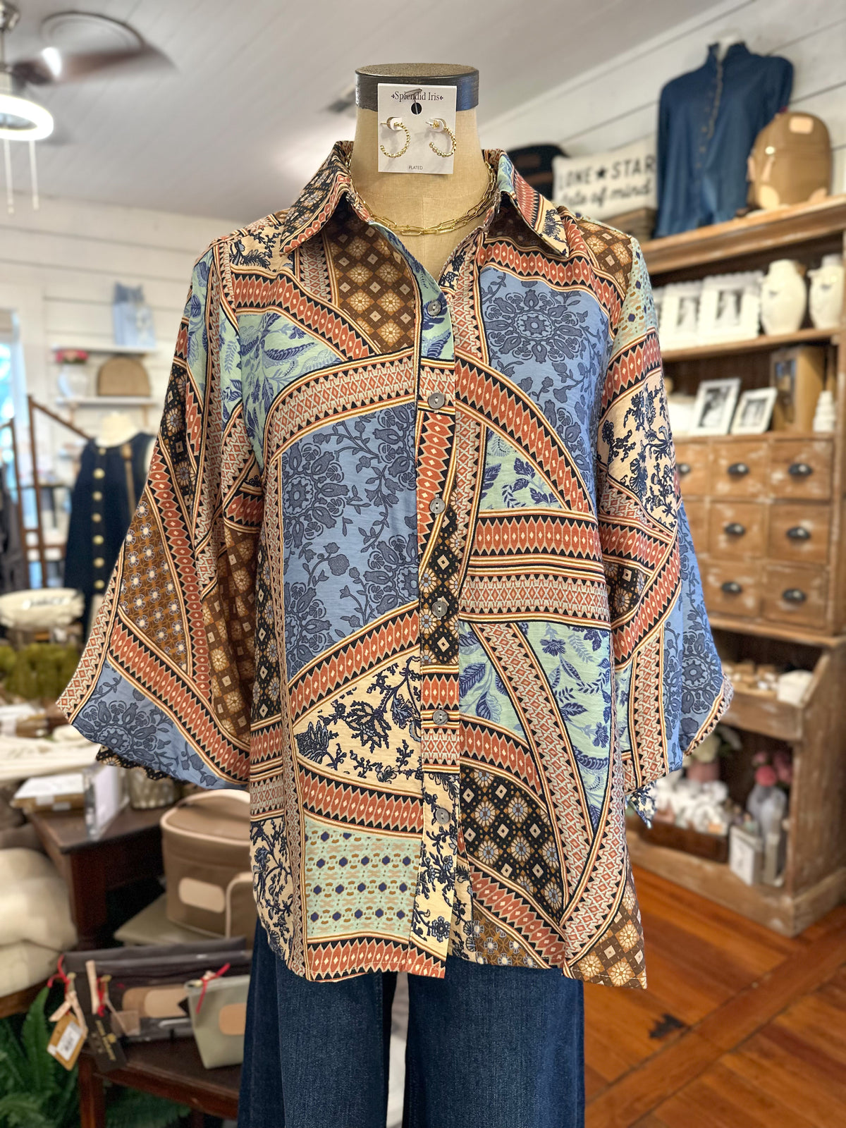 A multicolor patchwork print button-up shirt with three-quarter sleeves, displayed on a mannequin torso inside a retail store.