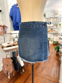 Blue denim skirt on a mannequin in a store setting with various items in the background.