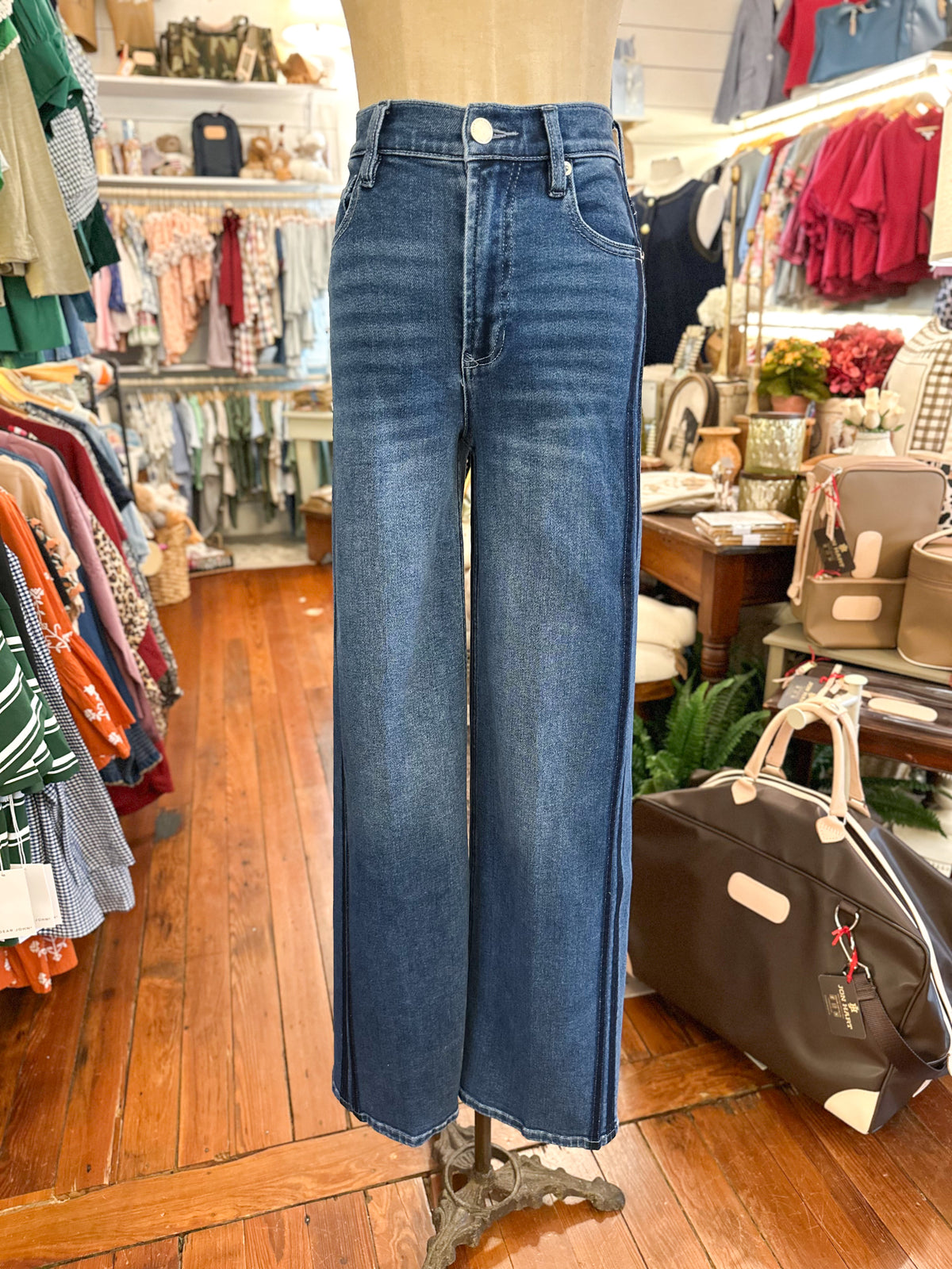 A pair of high-waisted, wide-leg blue denim jeans displayed on a mannequin inside a clothing boutique. The jeans feature a classic five-pocket design and a button closure.
