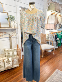 Mannequin wearing a floral blouse and blue jeans in a store setting with furniture and decor.