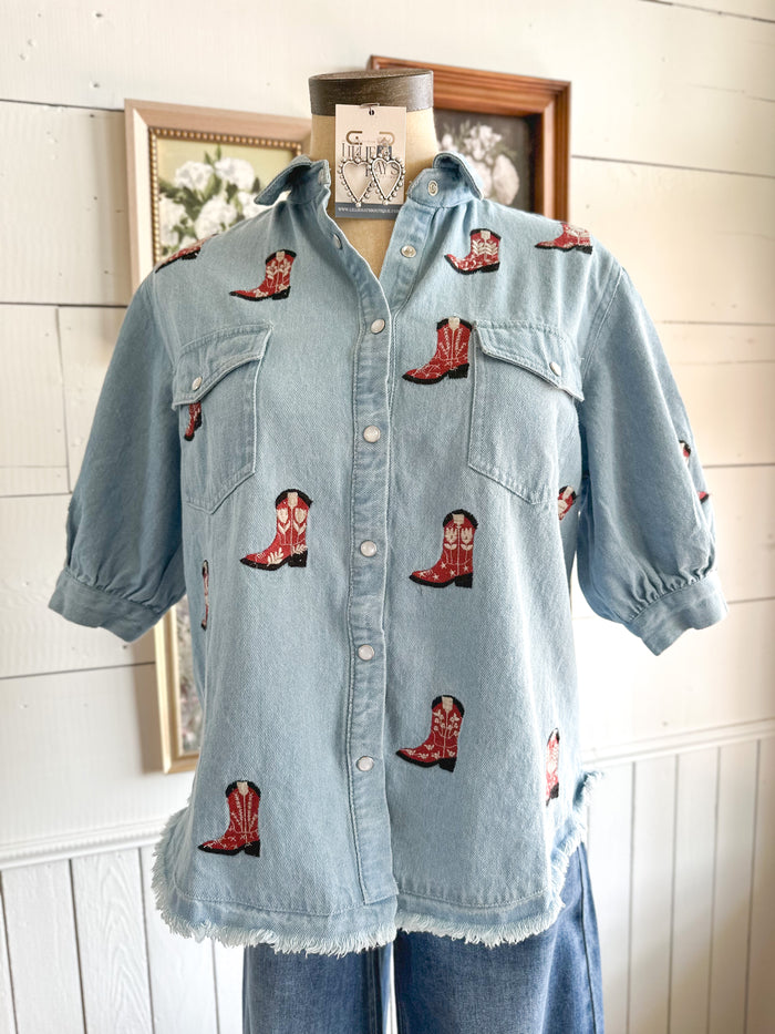 Light blue denim shirt with red cowboy boot patches on a mannequin against a white wall.