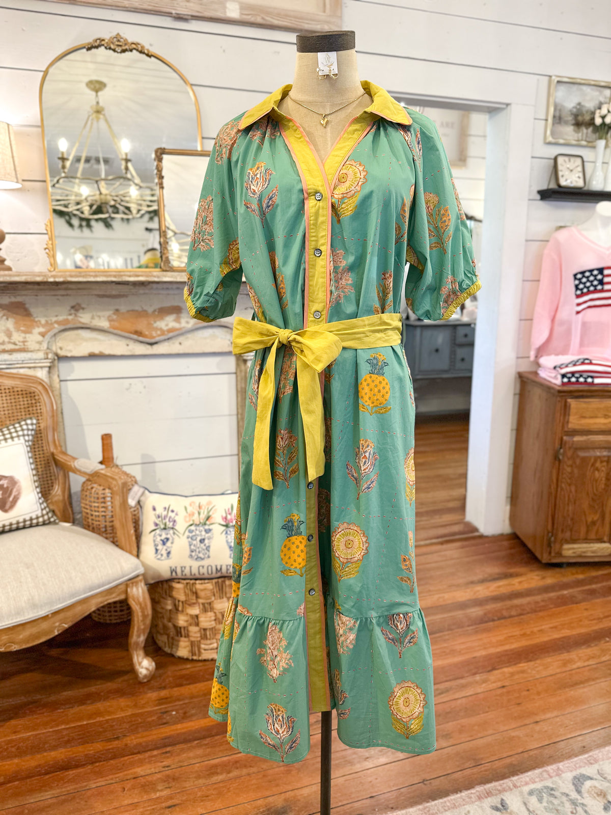Green dress with yellow accents on a mannequin in a room with wooden floors and furniture.