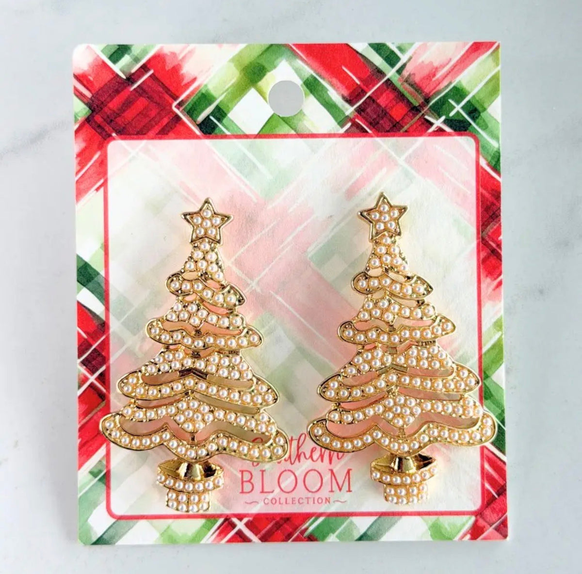 A pair of gold Christmas tree stud earrings embellished with small white pearls, presented on a decorative retail backing card with a red, green, and white plaid design. The backing card features the brand name 'BLOOM'.