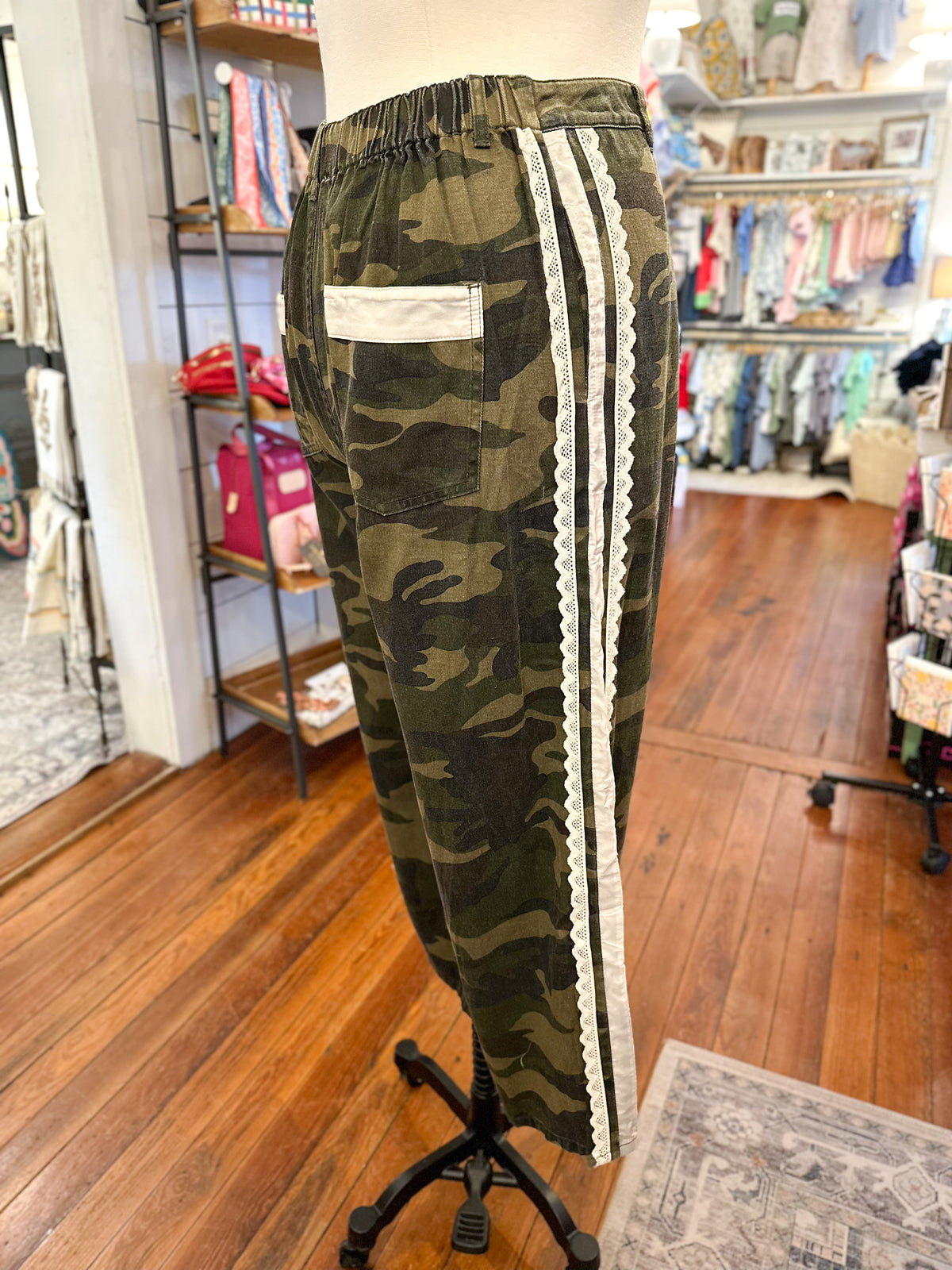 Camouflage pants with white lace stripes on a mannequin in a store setting
