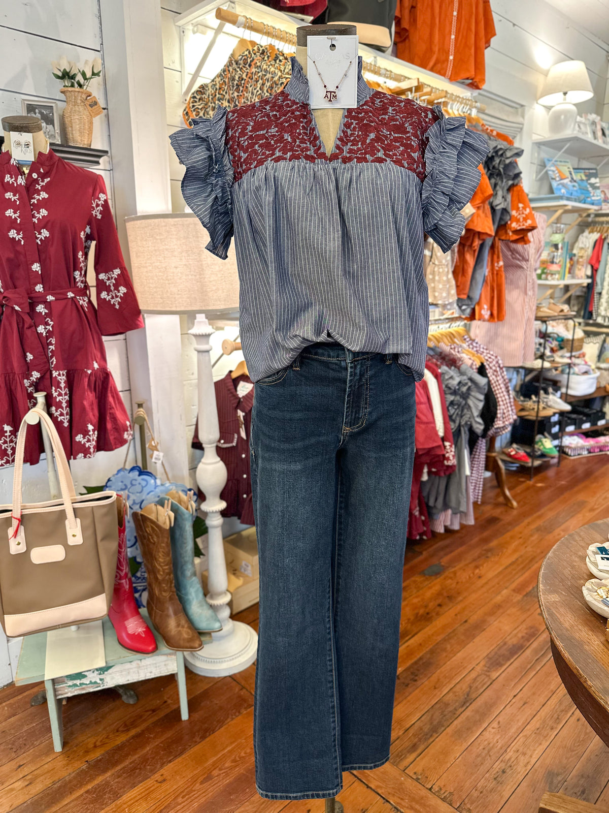 A mannequin in a clothing boutique wearing a blue and white vertically striped short-sleeve blouse with maroon embroidery.