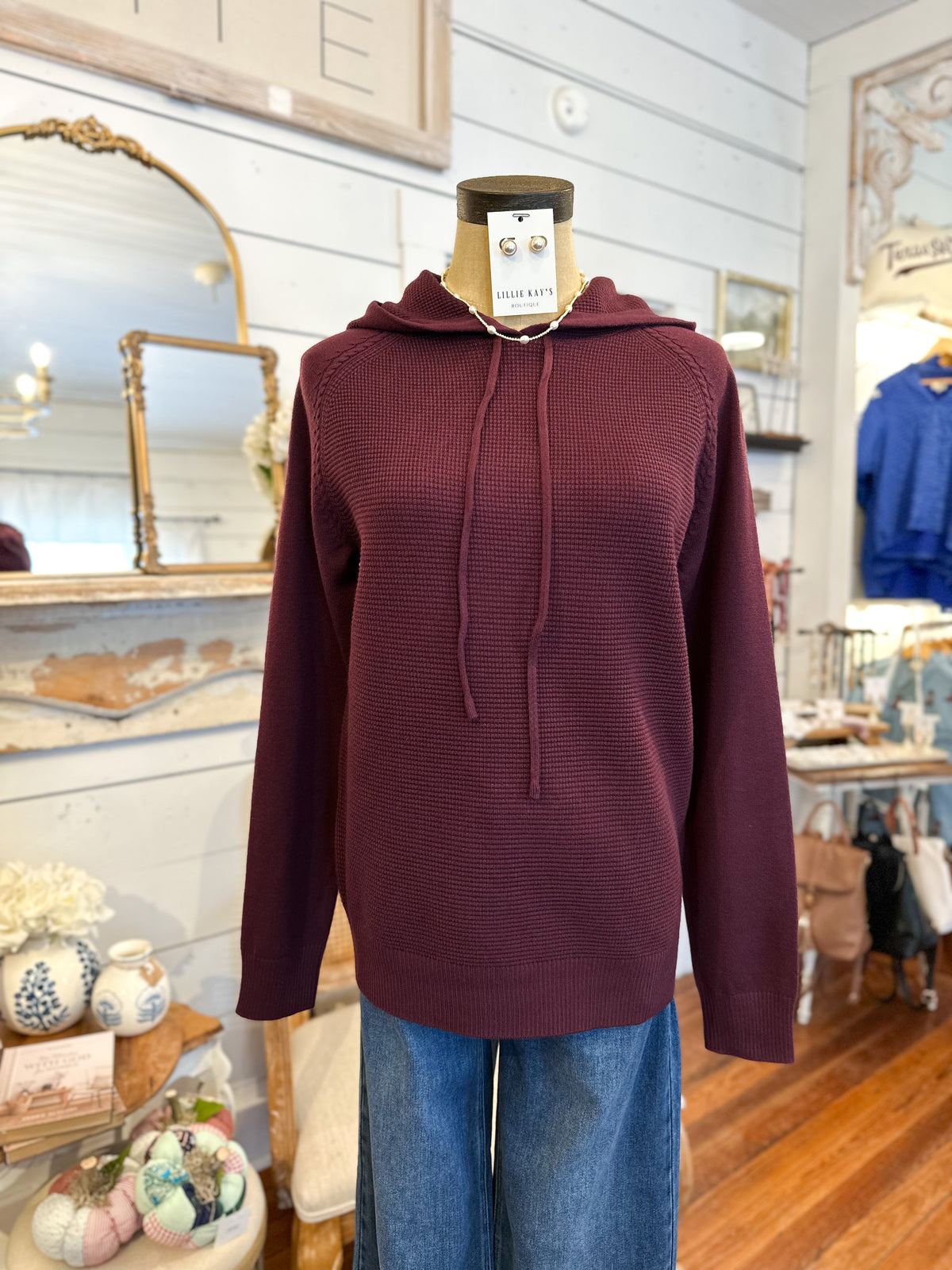 Maroon hoodie on a mannequin in a store setting with decor elements.