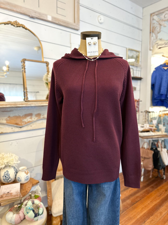 Maroon hoodie on a mannequin in a store setting with decor elements.