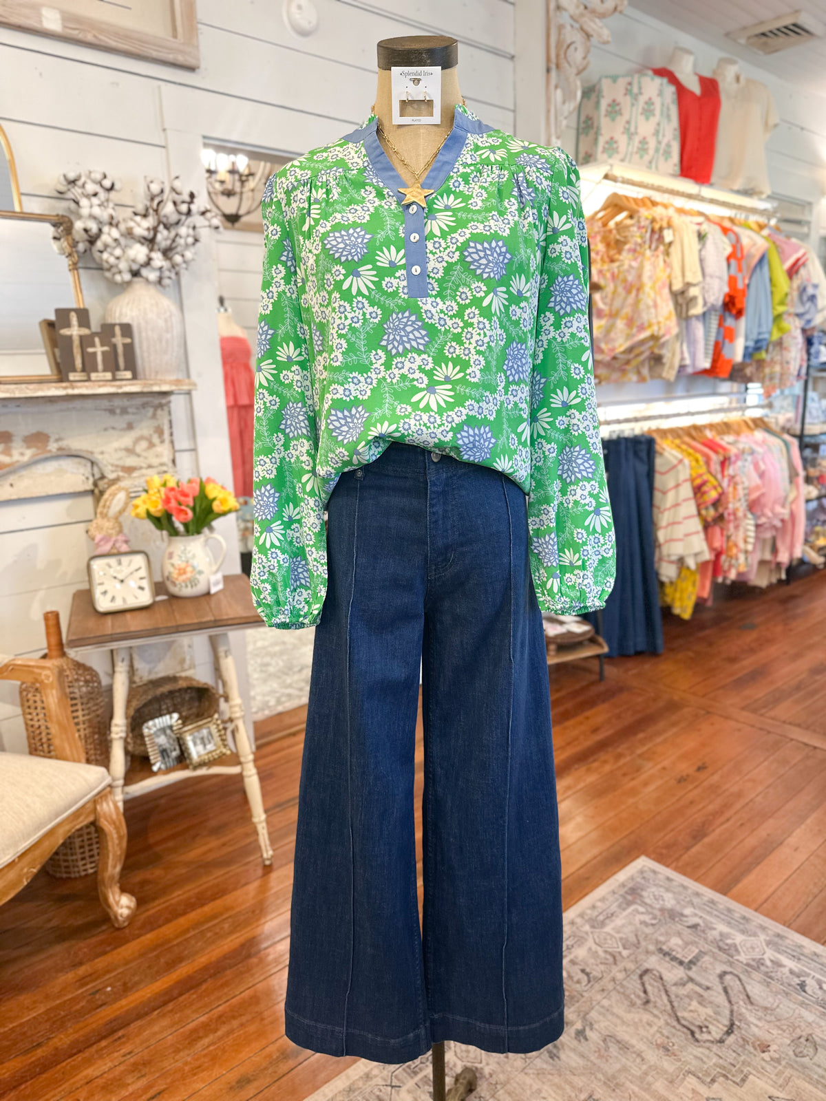 Green floral blouse and blue jeans on a mannequin in a store setting.