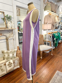 Purple dress on a mannequin in a store setting with wooden floor and various items in the background