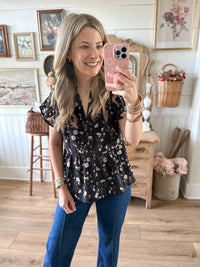 Woman taking a mirror selfie in a floral top and blue jeans in a home setting.