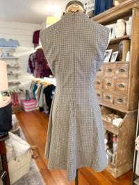 A sleeveless A-line dress with a small-scale black and beige windowpane check pattern, displayed on a mannequin in a boutique setting.