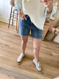 Person wearing denim shorts and white sneakers on a wooden floor.