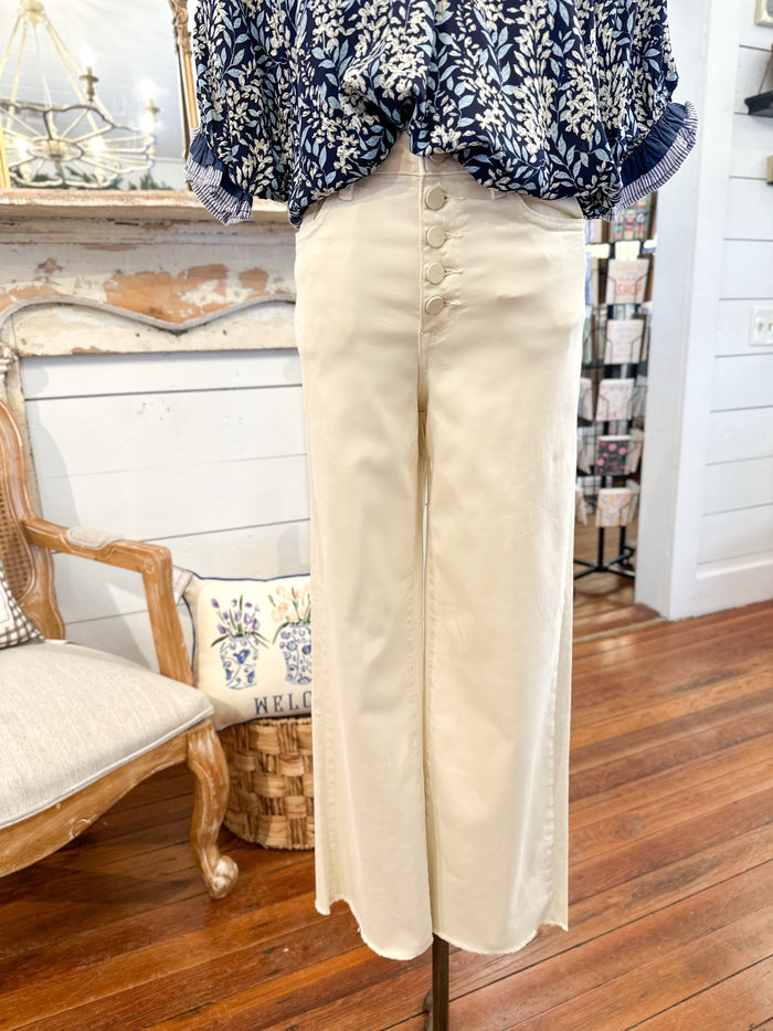 mannequin a blue patterned blouse and beige pants in a room with wooden floor and white walls.