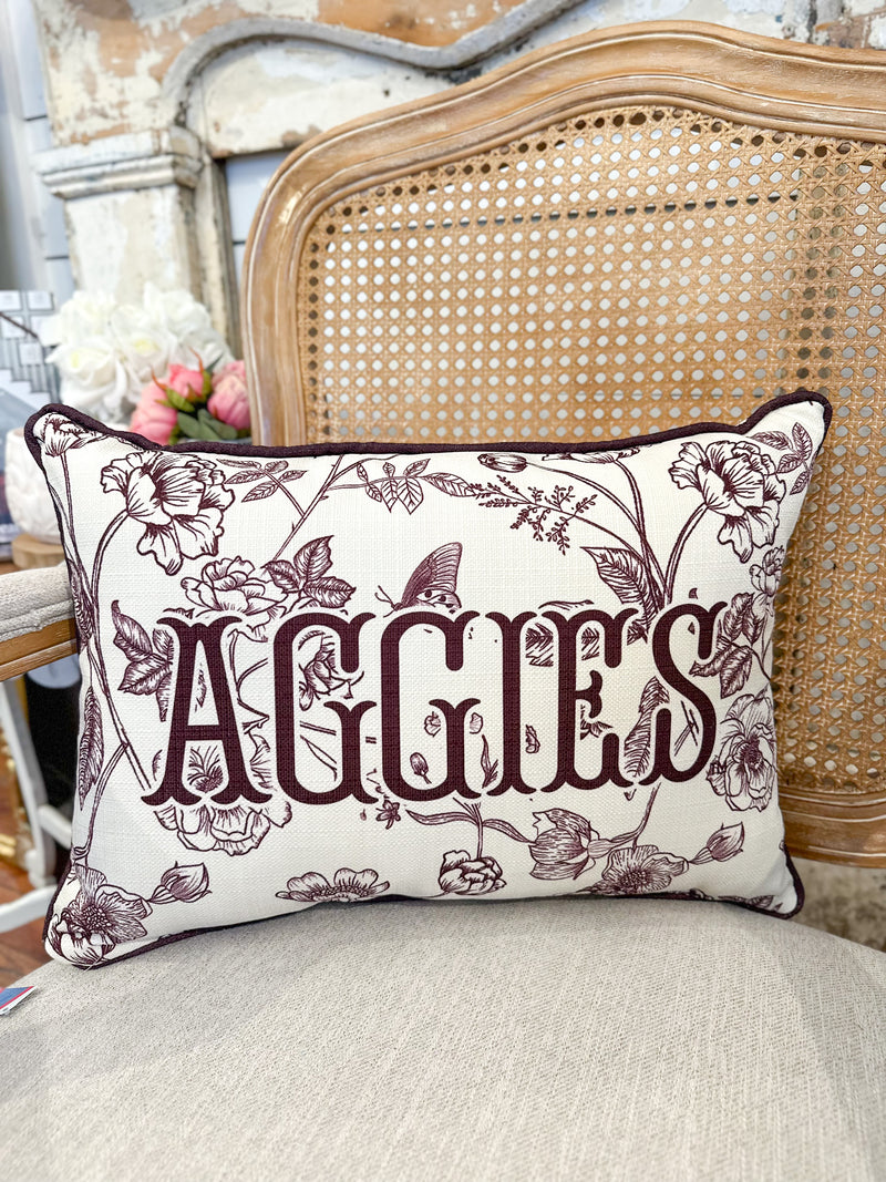 Decorative pillow with floral design and 'AGGIES' text on a chair.
