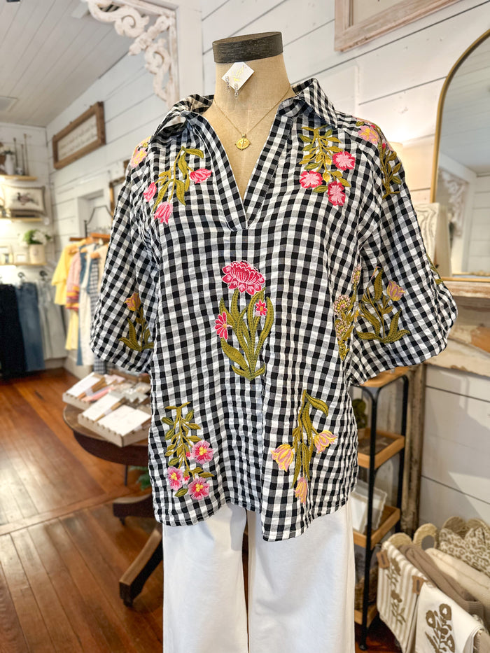 Black and white checkered blouse with floral embroidery on a mannequin in a store setting.