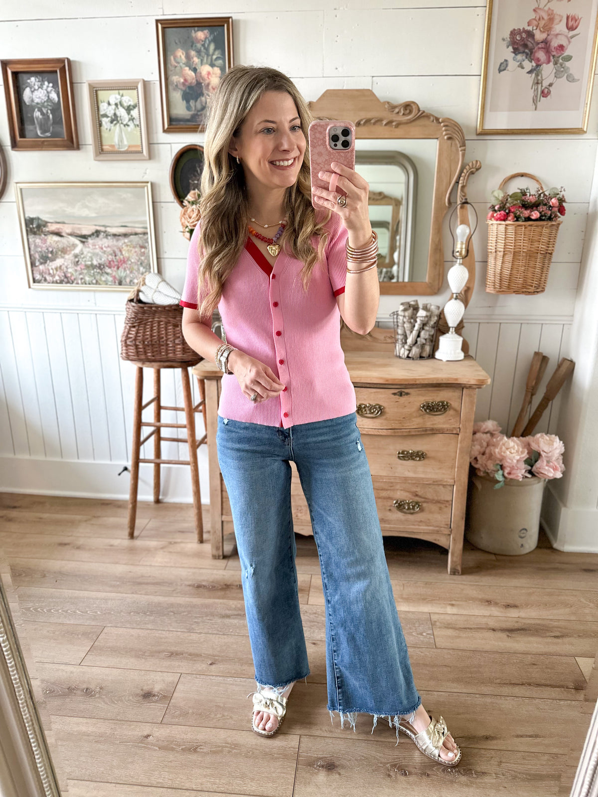 Woman taking a mirror selfie wearing a pink shirt and blue jeans in a home setting.
