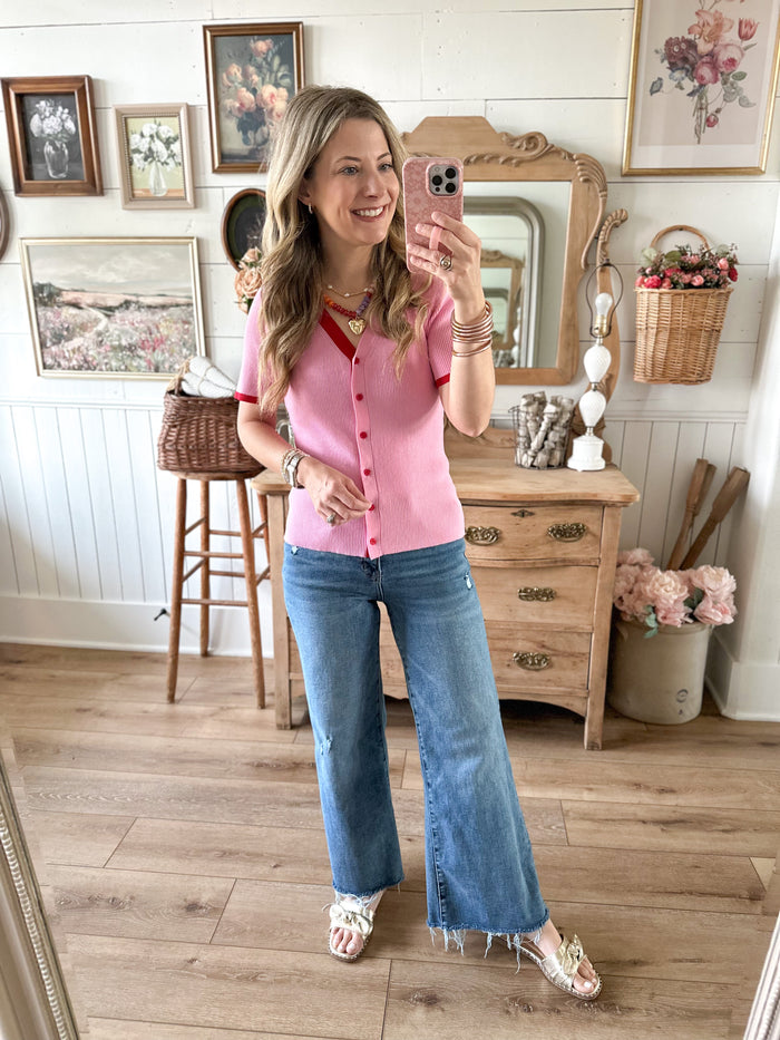 Woman taking a mirror selfie wearing a pink shirt and blue jeans in a home setting.
