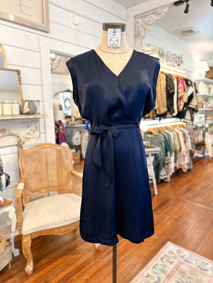 Navy blue dress on a mannequin in a store setting with wooden floor and chairs.